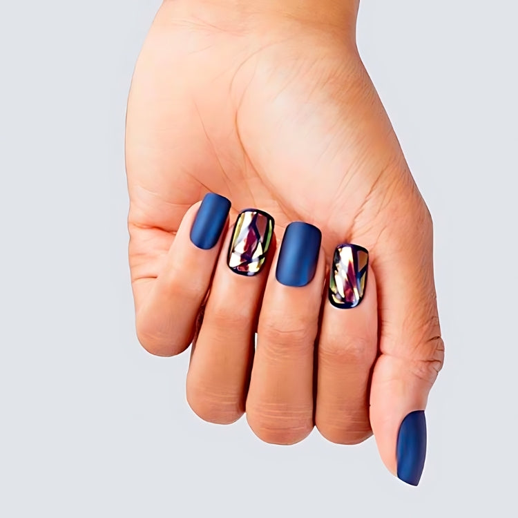 Glam Fantasy Nails - Tan Lines met een matte blauwe afwerking en kleurrijke accentnagels in een hand.