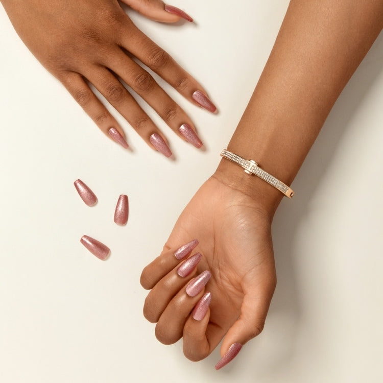 Gel Fantasy Magnetic - West Coast in glanzend rosegoud, met kunstnagels en een elegante armband op een hand.